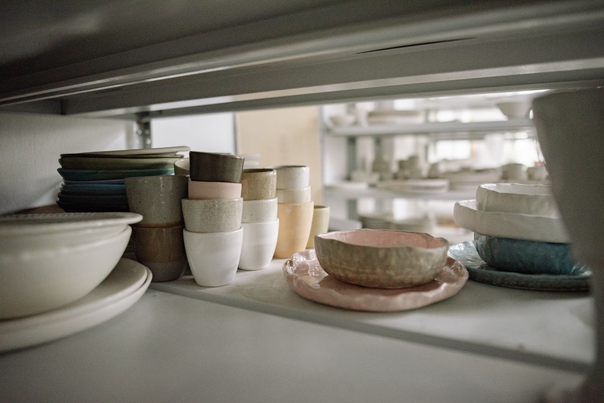 Handmade ceramic cups, bowls and plates arranged on a studio shelf