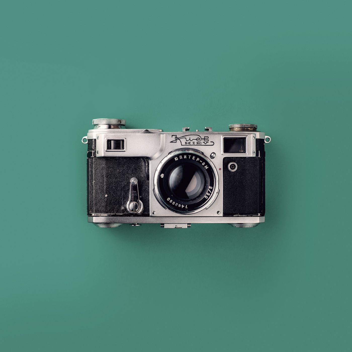 A vintage rangefinder camera photographed from above on a teal background