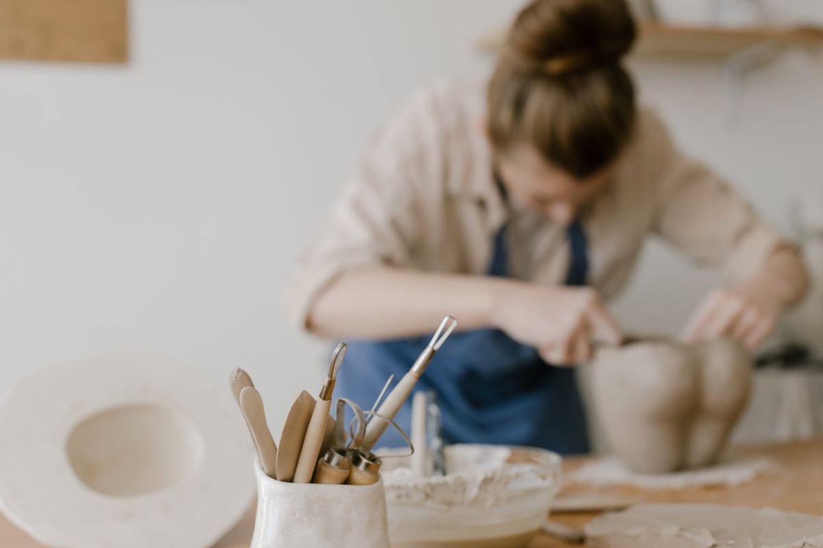 Pottery tools in the foreground with a woman shaping a clay vessel behind them