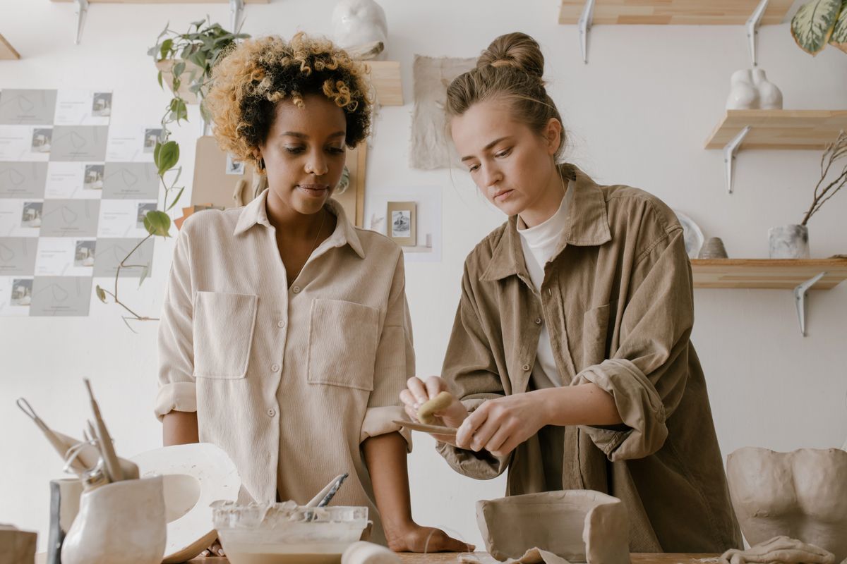Two women working with clay together at a pottery studio table