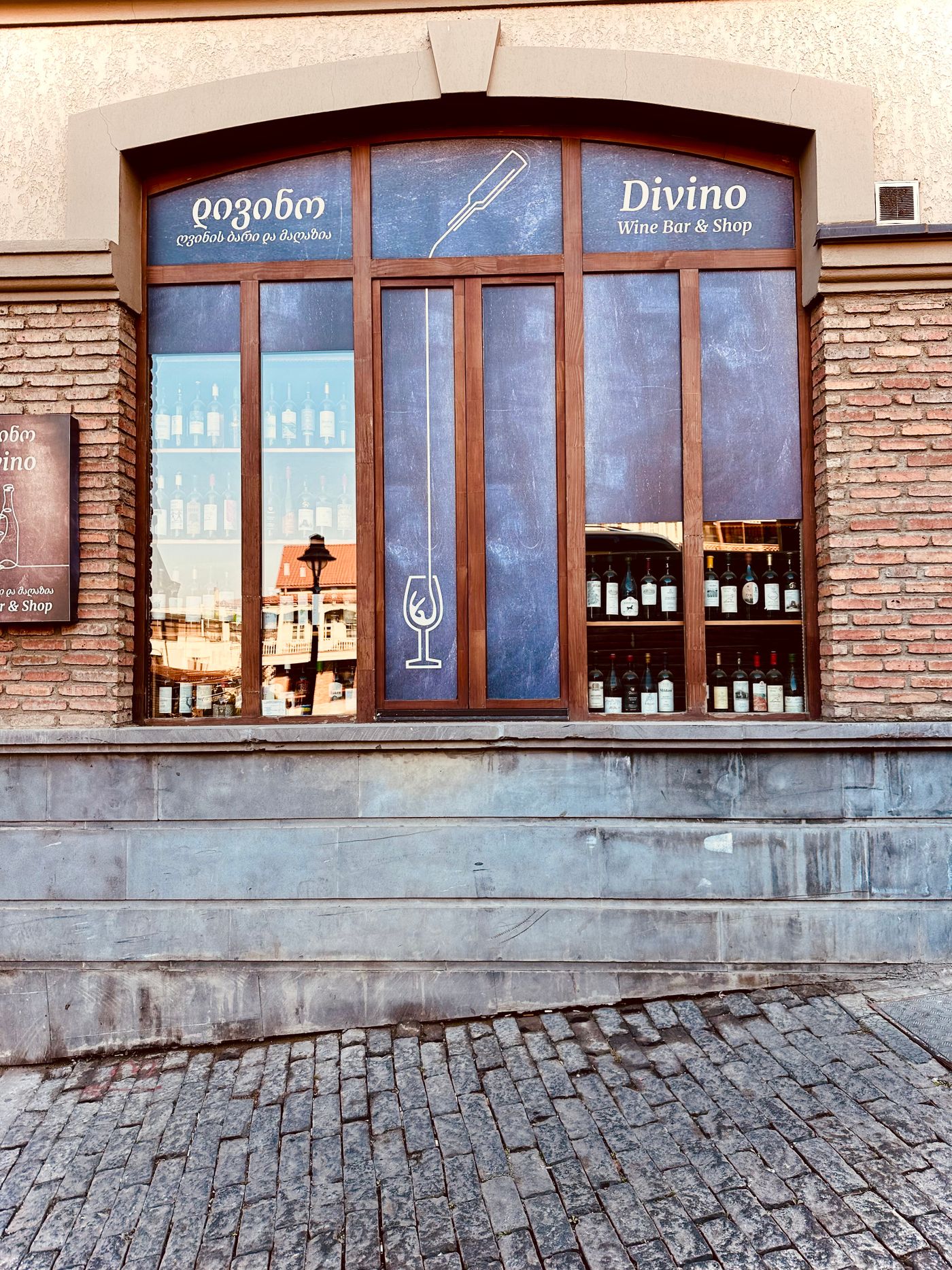 Street-level wine shop window with bottles on display and a cobblestone sidewalk