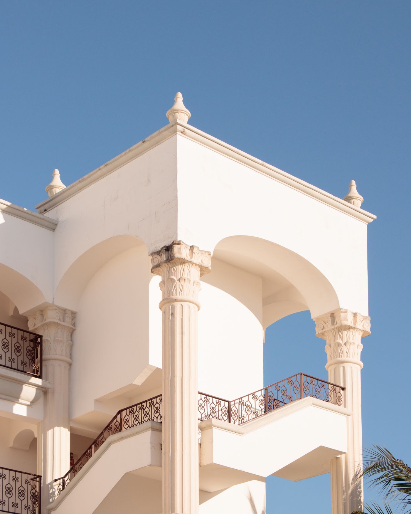 White building with arched columns and iron railings against a clear blue sky